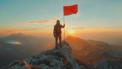 an-individual-in-red-reaches-the-summit-triumphantly-planting-a-red-flag-against-a-dramatic-mountain-backdrop