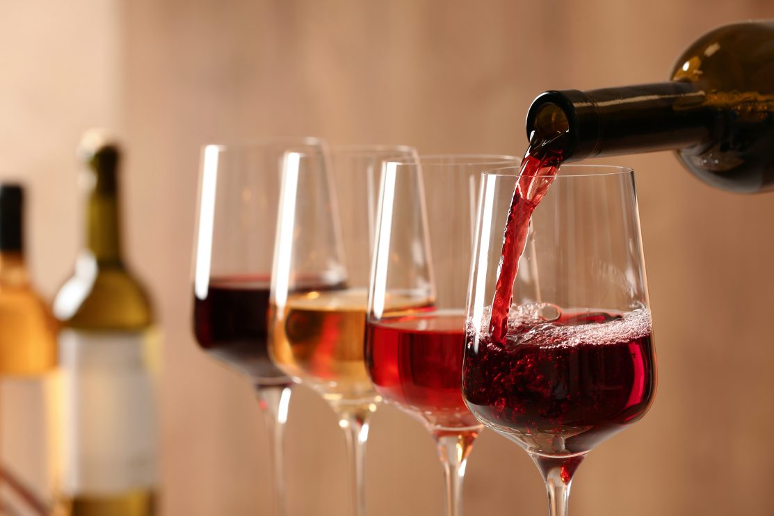 pouring-wine-from-bottle-into-glass-on-blurred-background-close