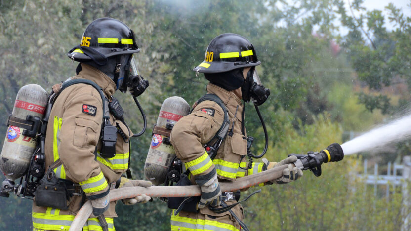 Two firefighters holding a fire hose spraying water