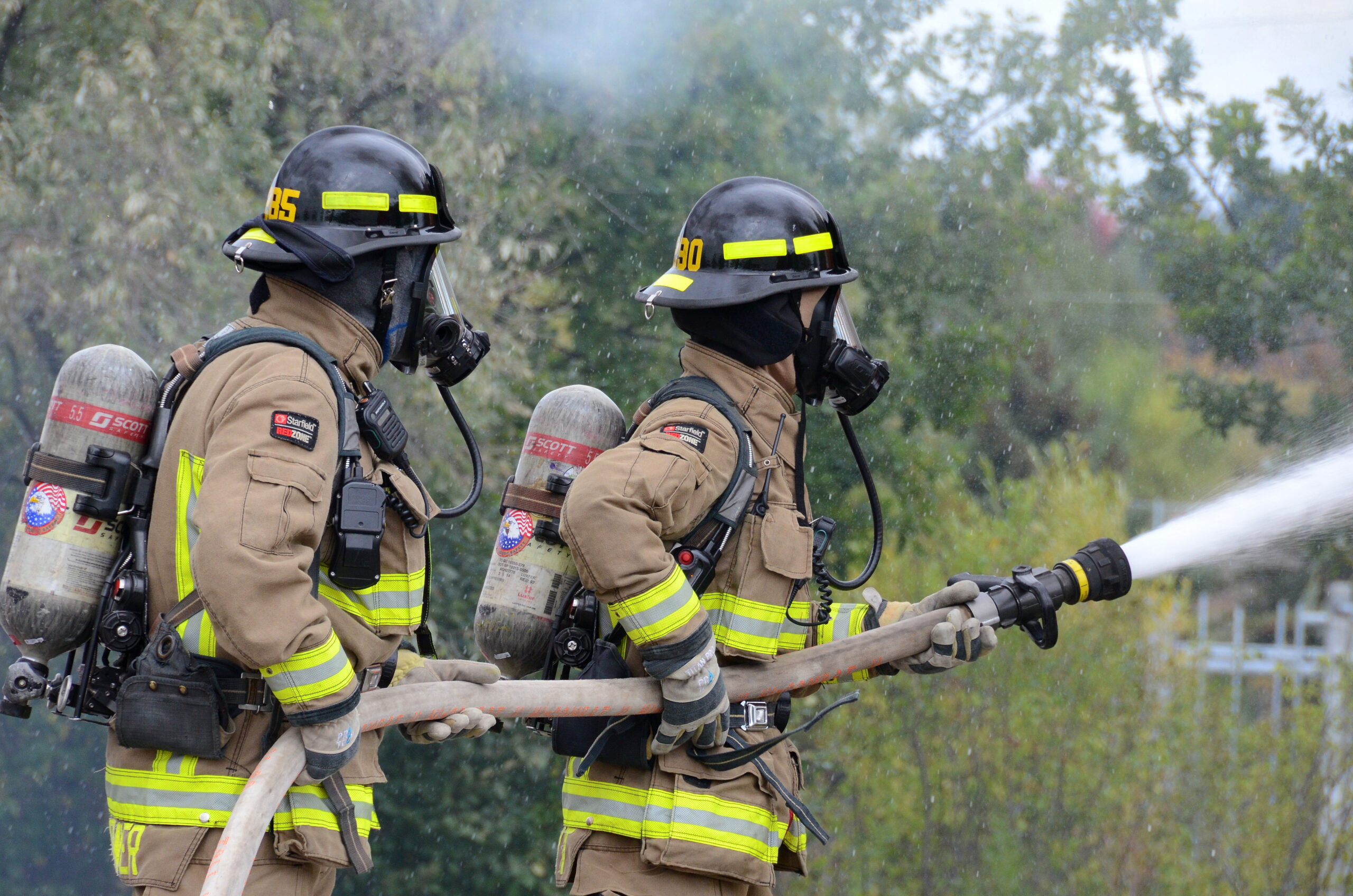 Two firefighters holding a fire hose spraying water